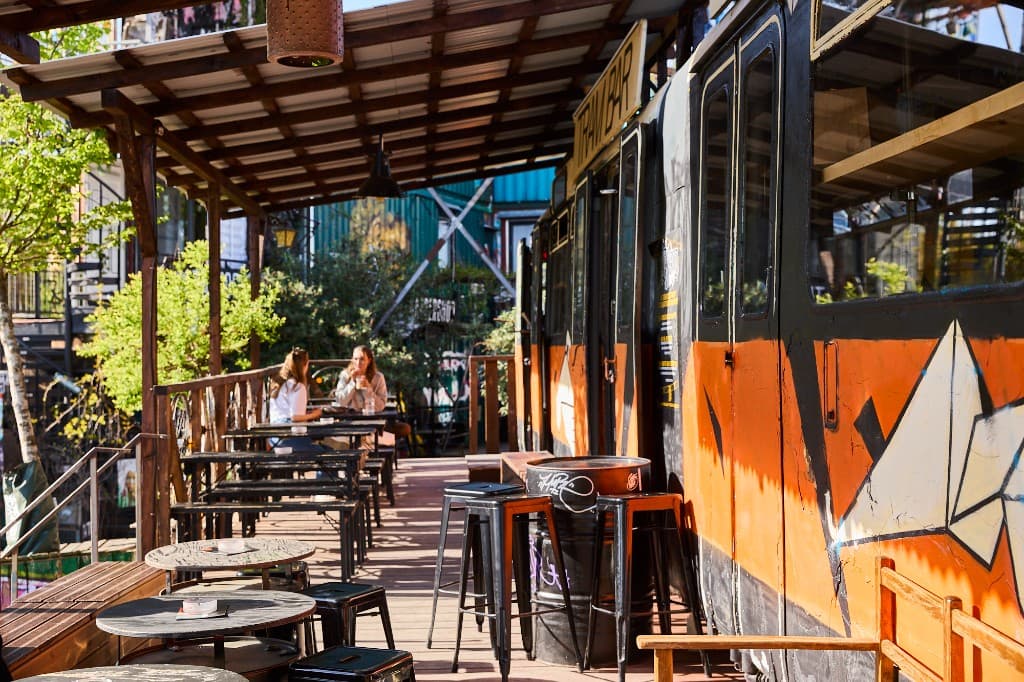 Sonnige Terrasse mit Tischen neben dem orangefarbenen Waggon